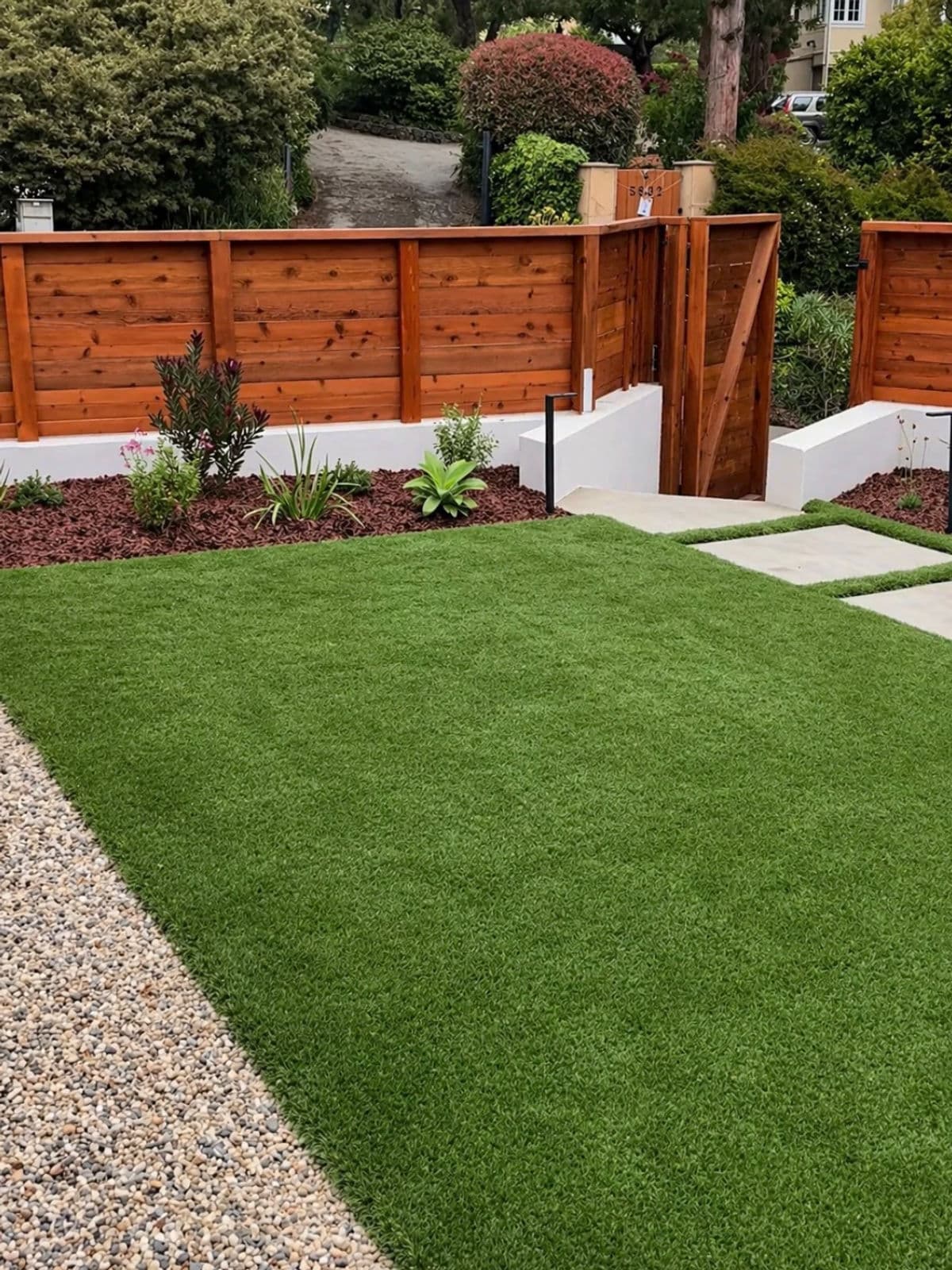 Artificial turf bordered by decorative gravel, planting, fencing, and concrete pads