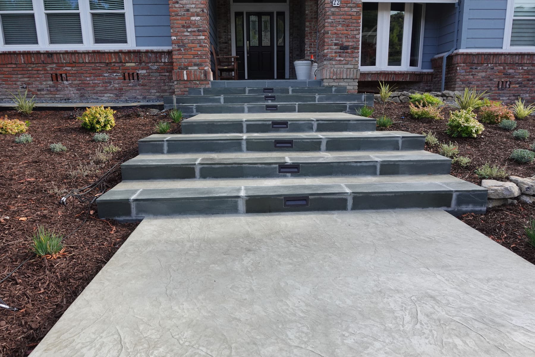 Concrete entry walk and broad steps framed by new planting and integrated step lights