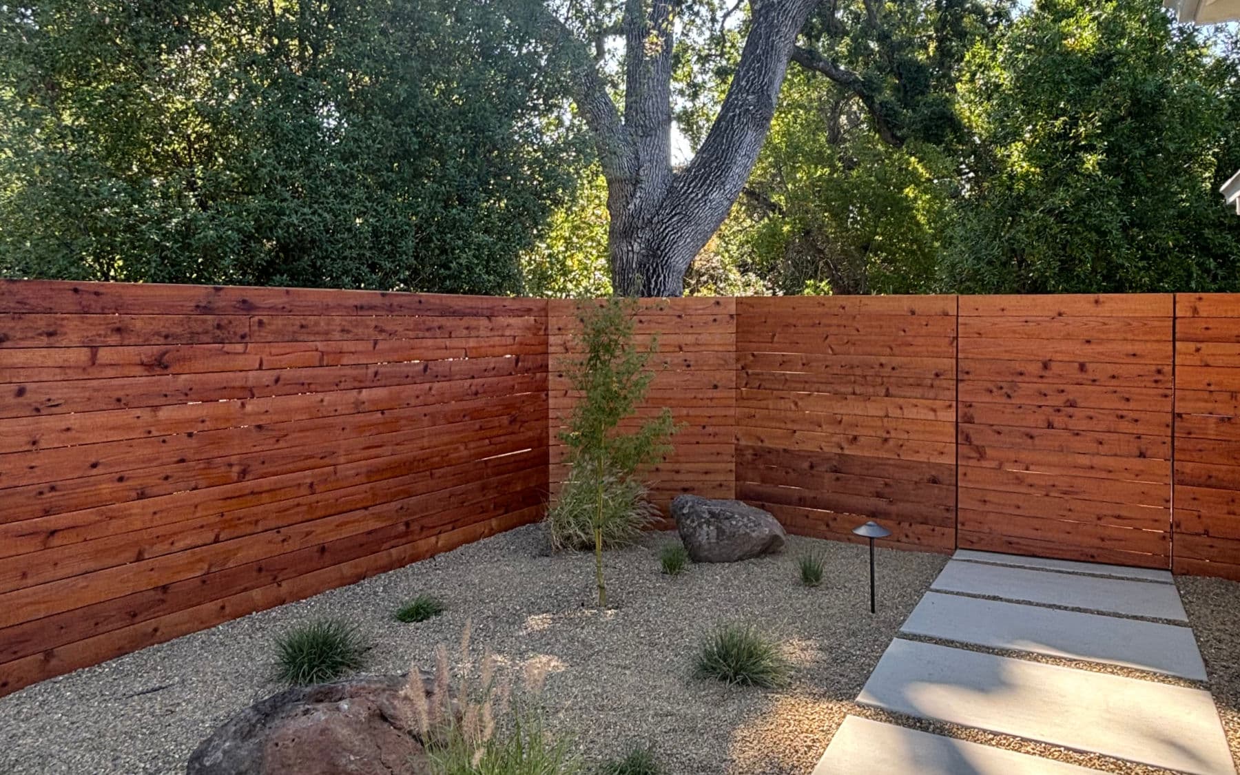 Horizontal wood privacy fence beside gravel planting and concrete stepping pads