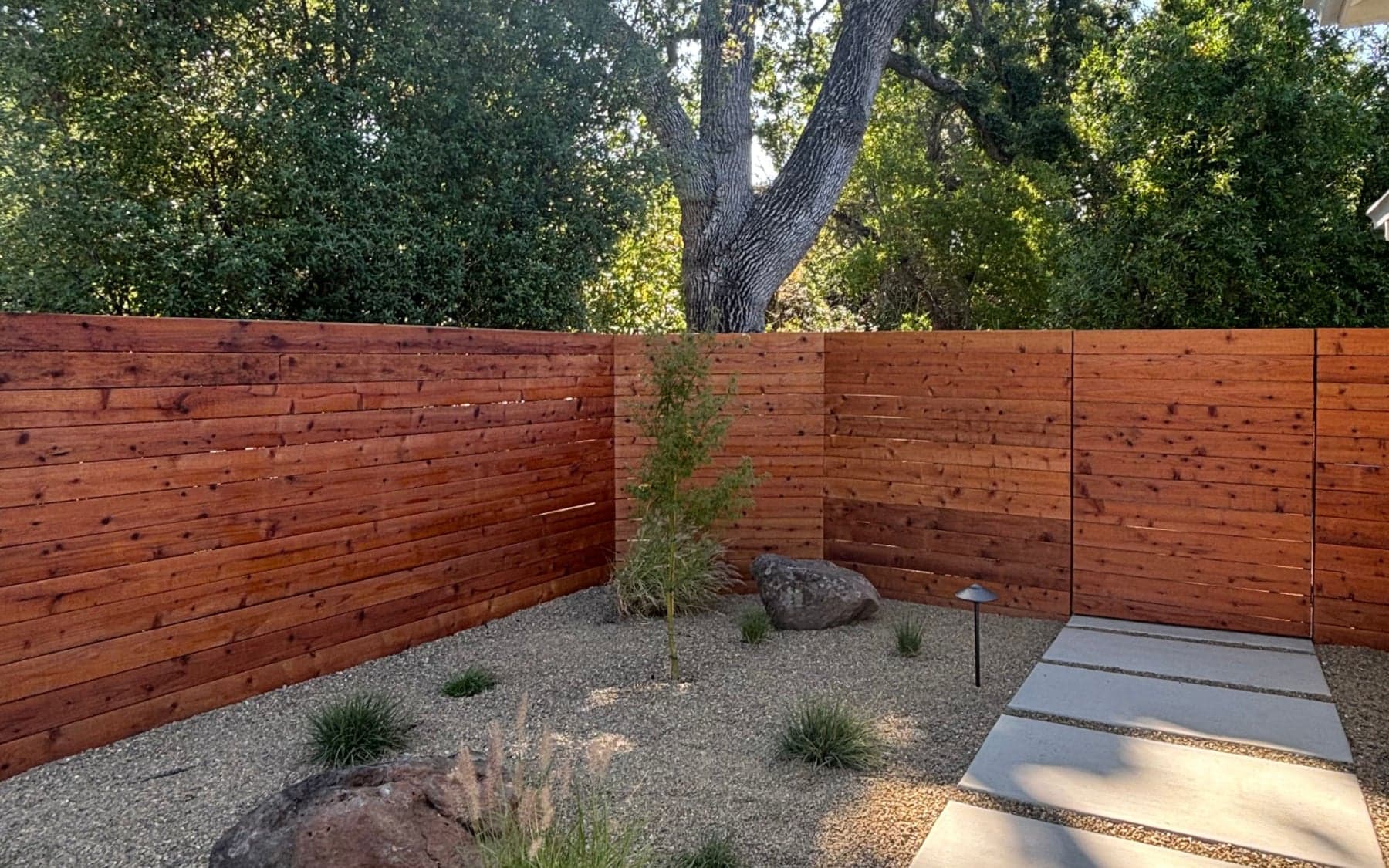 Horizontal wood privacy fence beside gravel planting and concrete stepping pads